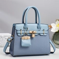 Close-up of light blue leather tote with woven texture, golden padlock, and mini bag charm - Blue