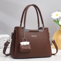 Dettaglio borsa a mano in pelle marrone con fibbie argentate e mini ciondolo decorativo - Marrone