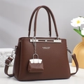 Close-up of brown lychee leather handbag with brand logo and mini charm accessory - Brown
