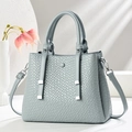 Detail of light blue-grey handbag with woven texture and silver hardware in minimalist setup - Blue