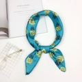 Sciarpa di seta color teal con stampa di ananas gialli annodata su un tavolo bianco - Ananas Blu Lago
