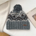 Primer plano detallado de gorro de punto gris con patrones geométricos y un gran pompón - Gris claro