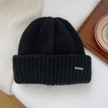 Primer plano de gorro de punto negro con logo metálico plateado sobre bandeja de madera - Talla Única (22*25cm) / Negro (Etiqueta de Metal)