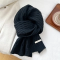 Close-up of thick black knit scarf texture with a white logo label on a cozy background - Black
