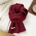 Detailed close-up of dark red wool blend scarf with chunky knit texture and white label - Burgundy