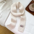 Close-up of cream knitted scarf with vintage label detail and ribbed texture pattern - Beige