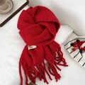 Detail shot of a vibrant red knitted scarf with tassels and white brand label on a cozy setup - 28*210cm / New Year Red