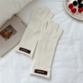 Detalle de guantes de punto blanco roto con etiqueta de cuero marrón sobre tela suave - Talla única / crema