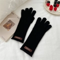 Close-up of black knitted gloves with a brown leather logo patch on soft white fabric - One Size / Black