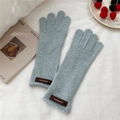 Detail of light blue knitted glove with a brown leather logo patch on white fabric - One Size / Blue