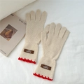 Détail de gants en tricot crème avec bordure festonnée rouge et étiquette en cuir brun - Beige