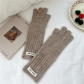 Close-up of brown ribbed knit gloves with white logo tag on white fabric background - Coffee