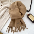 Detalle de bufanda de punto color camello con flecos, logo metálico y textura suave - Camel