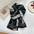 Detail eines weichen Strickschals mit schwarz-weißem Rautenmuster und Markenetikett - Schwarz
