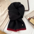 Detailed close-up of a black wool scarf with a red ribbed edge and gold metal emblem - Black