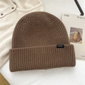 Detalle de gorro de lana marrón oscuro con textura de punto de canalé grueso sobre tela blanca - Marrón