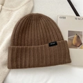 Detail of a brown ribbed wool beanie featuring a 100% wool composition tag on knit fabric - Brown