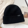 Close-up of the 100% wool label on a black ribbed knit beanie with high-quality texture - Black