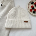 Detailed texture of white ribbed knit beanie with leather label and decorative berries - Creamy White
