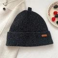 Detailed knit texture of a dark grey wool beanie with a leather logo and ring detail - Patterned Black
