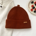 Detailed macro view of warm brown ribbed knit wool beanie with leather patch on white surface - Orange