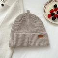 Close-up of oatmeal knit beanie with ribbed texture and brown leather brand label - 28*25cm / Beige Grey