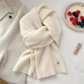 Close-up of cream wool knit scarf texture with vertical stripes and silver logo plate - Creamy White