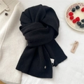 Detailed texture of a black ribbed knit wool scarf with a metallic logo and washing label - Black