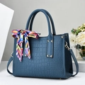 Detail einer dunkelblauen Handtasche mit Krokoprägung, Nieten und dekorativem Seidenschal - Blau