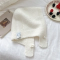 Detalle de capucha de punto crema con perla y etiqueta azul sobre una tela suave - crema