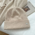 Detailed knit texture of beige beanie featuring a small oval silver metal logo tag - One Size / Off White