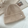 Detailed texture of beige ribbed knit beanie featuring a small round metal logo plaque - One Size / Off White