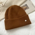 Close-up of a dark brown knitted beanie with fine vertical ribs and silver logo detail - One Size / Orange