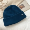 Detail of navy knit beanie with silver brand logo button on cozy lifestyle background - One Size / Navy Blue