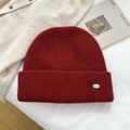 Detalle del gorro de punto burdeos con textura acanalada y placa metálica de logo - Talla única / Burdeos