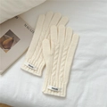 Detalle de guantes de punto trenzado crema con etiqueta sobre fondo de algodón suave - crema