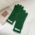 Detalle de guantes de punto trenzado verde oscuro sobre un fondo de tela blanca suave - Verde
