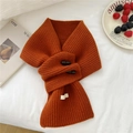 Close-up of caramel knit wool scarf with decorative double buttons and white fabric label - Orange