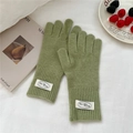 Detalle de guantes de punto verdes con puños acanalados y etiquetas en fondo de tela blanca - Talla única / Verde Hierba