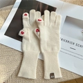 Close-up of beige knit gloves featuring red heart embroidery and brown leather brand label - Cream