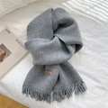 Gray knitted scarf with fringe and Hand Made leather label on white bedding background - Gray