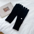 Close-up of black knitted gloves with ribbed cuffs and silver metal logo on white fabric - One Size / Black