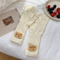 Detalle de guantes de punto crema con puños acanalados y etiqueta de cuero marrón en fondo blanco - Talla única / Beige