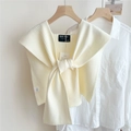 Dettaglio di uno scialle in maglia a coste crema annodato su camicia bianca - crema