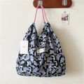 Detail of floral canvas tote bag with pink rope handles and brand label on a wall hook - Sticker Blue Flower Black