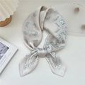 Off-white square silk scarf with blue paisley pattern tied in a bow on a white desk - Nude Paisley