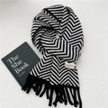 Close-up of winter knit scarf featuring black and white herringbone pattern with fringe - Black