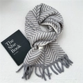 Detail of grey and white herringbone knit scarf with soft fringe and stylish brand tag - Gray