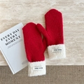 Close-up of red knit mittens with white plush cuffs and Doria Dore logo label on tabletop - Red
