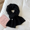 Close-up of black ribbed knit scarf with woven label on soft white bedding texture - Black